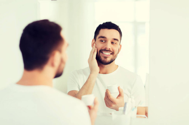 happy young man applying cream to face at bathroom - Foto, Imagem