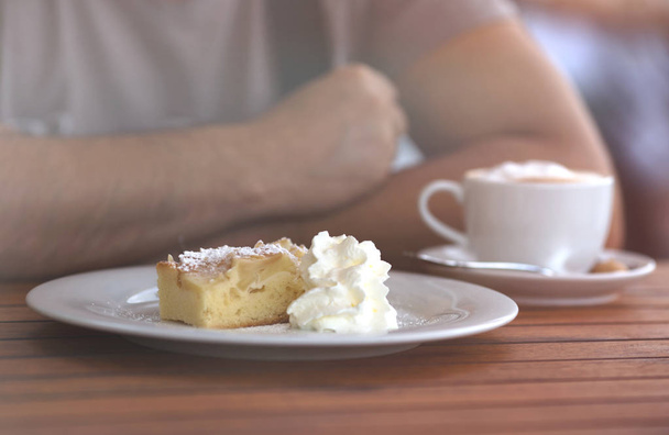クリーミーな甘いケーキ、木のテーブルにコーヒーのカップの部分を持ってカフェに座っている人にクローズ アップ. - 写真・画像