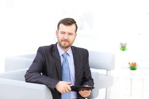 Happy businessman sitting on the sofa looking at camera in the office - Fotó, kép