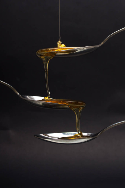 Honey pouring from spoon against a dark background - Φωτογραφία, εικόνα