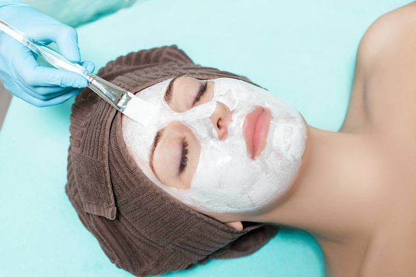 beautician applies face mask on beautiful young woman in Spa salon. cosmetic procedure skin care. Microdermabrasion - Photo, Image
