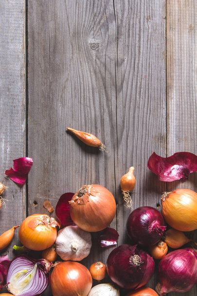 Several kinds of different onion bulbs lying on an old wooden table. - Foto, imagen