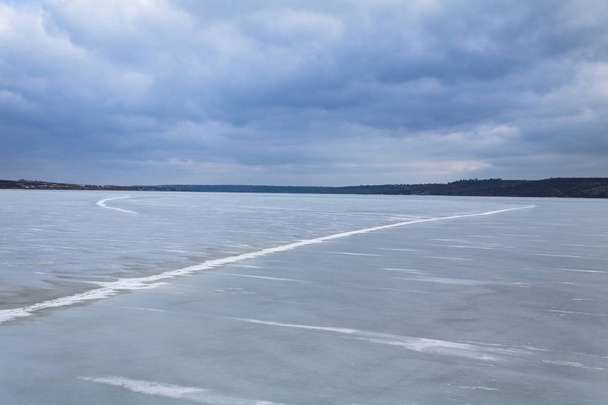 Παγωμένη λίμνη τη χειμερινή μέρα. Μια μεγάλη γραμμή κρακ στην επιφάνεια της λίμνης. Σύννεφα καταιγίδας - Φωτογραφία, εικόνα