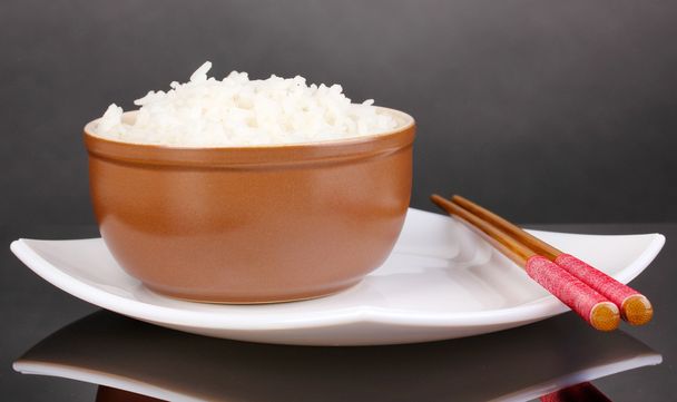 Bowl of rice and chopsticks on plate on grey background - Foto, Bild