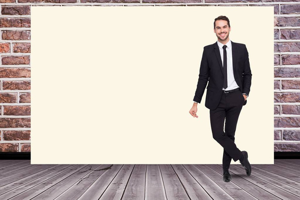 Portrait of smiling businessman standing by blank white billboard against brick wall - Φωτογραφία, εικόνα