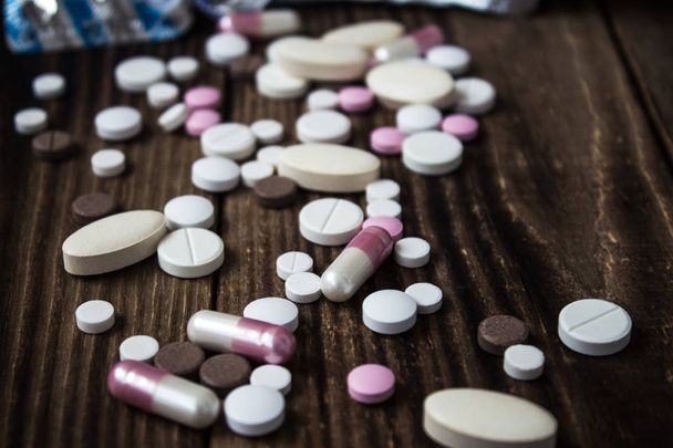pile of pills of different sizes on a wooden background - Photo, Image