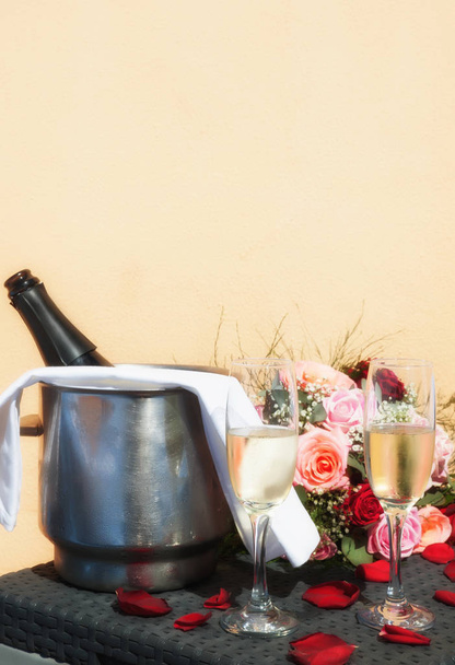 Mesa exterior románticamente equipada con botella de champán sobre hielo y flautas de champán completas
 - Foto, imagen