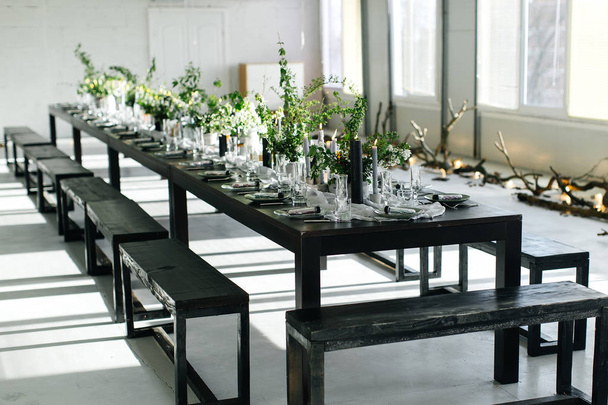 Elegante mesa, loft. Habitación de diseño en estilo loft. Mesa negra, sillas, platos, velas. Frascos con verduras
. - Foto, imagen