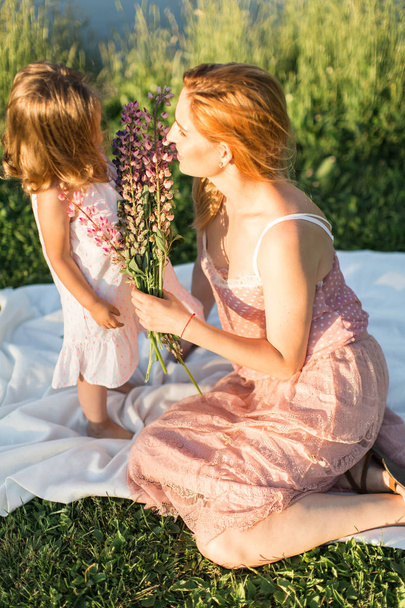 Mom and daughter are sitting on a rug by the lake - Photo, Image
