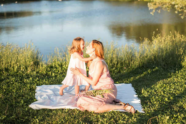 Mom and daughter are sitting on a rug by the lake - Foto, imagen