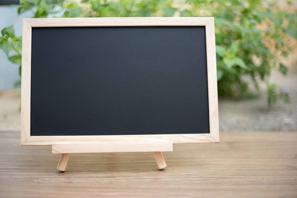  Black board on wood table top with sun and blur green tree boke - Foto, imagen