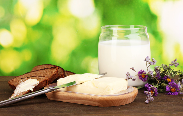 Butter on wooden holder surrounded by bread and milk on wooden table on natural background close-up - Valokuva, kuva