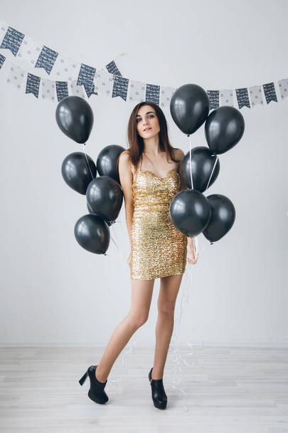 Girl in a gold dress with black balloons - Foto, Bild