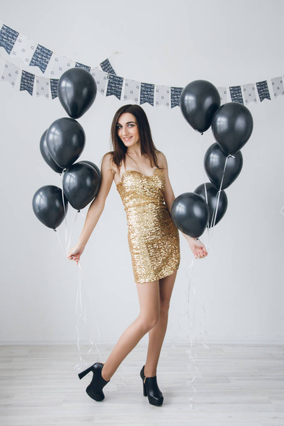 Girl in a gold dress with black balloons - 写真・画像