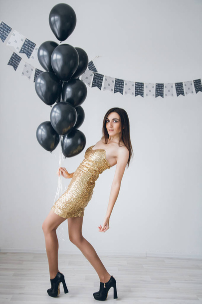 Girl in a gold dress with black balloons - Foto, afbeelding