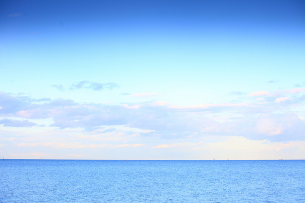 青い地平線の表面の海を残す曇りの青い空 - 写真・画像