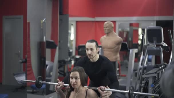 Entrenador ayudando a la mujer a levantar la barra en un gimnasio
 - Metraje, vídeo