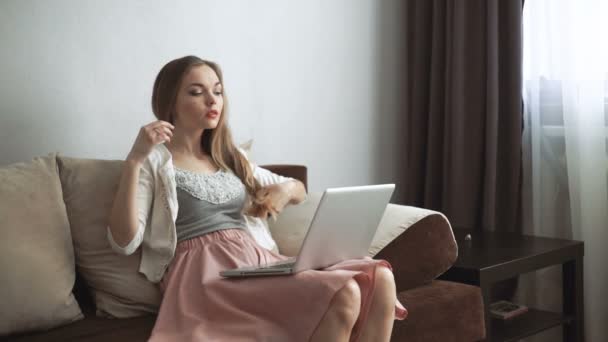 Young woman sitting on couch using laptop and smiling - Imágenes, Vídeo