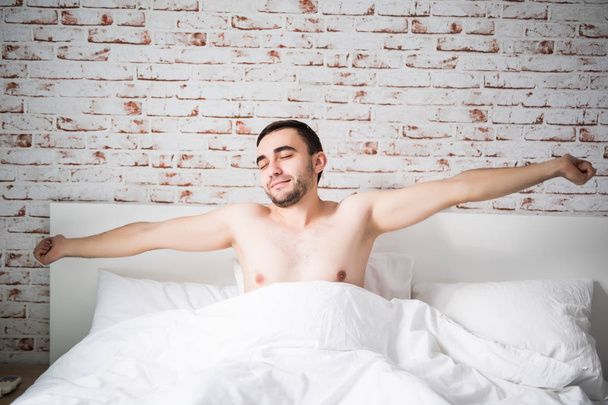 Χαρούμενος νεαρός άνδρας έχει ξυπνήσει μετά από ύπνο το πρωί ξαπλωμένη στο κρεβάτι - Φωτογραφία, εικόνα