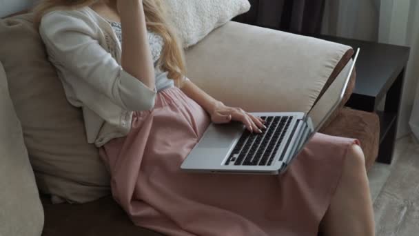 Mujer joven sentada en el sofá usando el ordenador portátil y sonriendo
 - Imágenes, Vídeo
