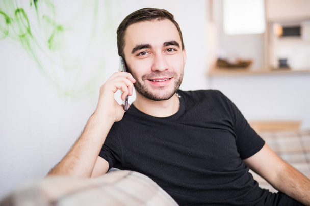 Красивий чоловік на мобільному телефоні сидить у вітальні
 - Фото, зображення