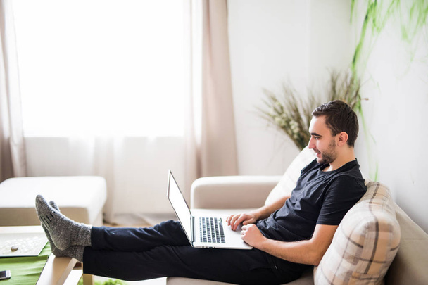 Giovane uomo che si rilassa sul divano con un computer portatile a casa
 - Foto, immagini