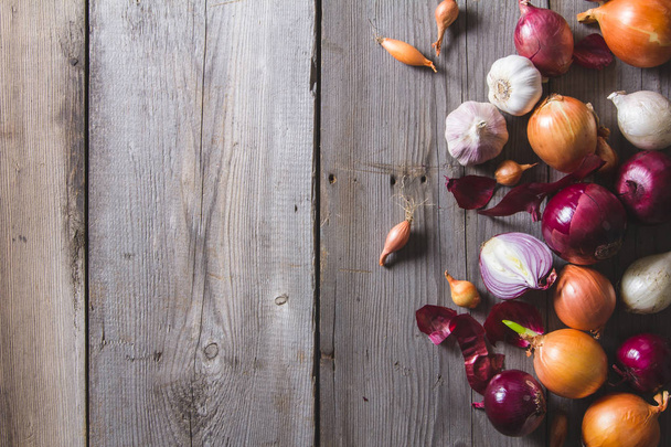 Several kinds of different onion bulbs lying on an old wooden table. - Photo, image