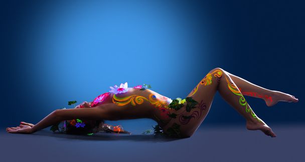 Beauty woman lay in glowing flowers under uv light - Valokuva, kuva