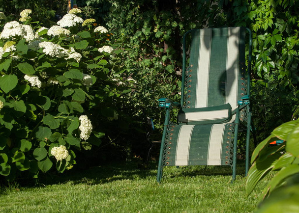 kannettava tuoli puutarhassa, mukava tuoli, yleensä verhoiltu, jossa on sivutuet henkilön käsivarsille
. - Valokuva, kuva
