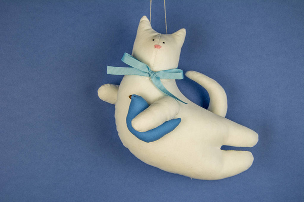 Ручной белый хлопок игрушка кошка летит на голубом небе с птицей в лапе / милые игрушки / котенок с простым луком-узел / закрыть задний план
  - Фото, изображение