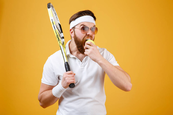 Hungry young tennis player bite tennis ball. - Foto, Imagen