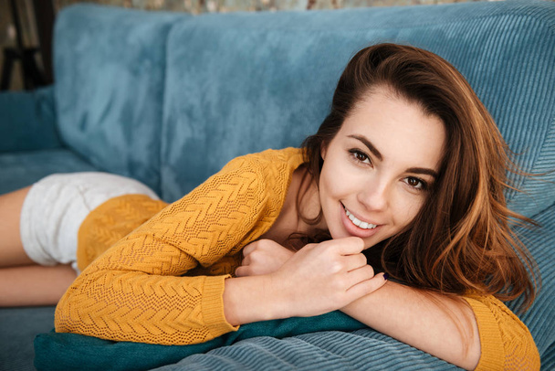 Smiling girl resting on a couch and looking at camera - Foto, Imagen