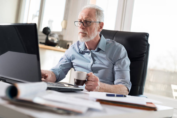 Portrait of senior businessman working on laptop, hard light - Photo, Image