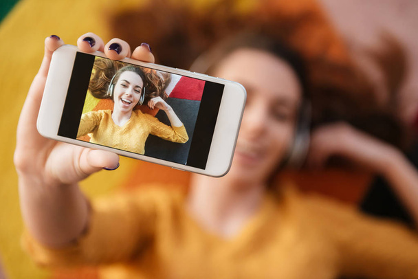 Top view of beautiful young woman in headphones making selfie - Foto, Imagen
