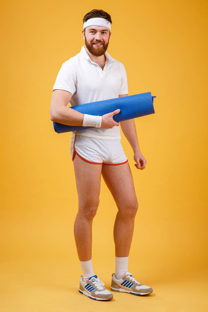 Full length portrait of a male athlete holding mat - Фото, изображение
