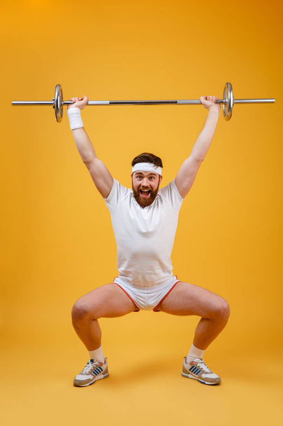Full length portrait of a fitness man squatting with barbell - Fotó, kép