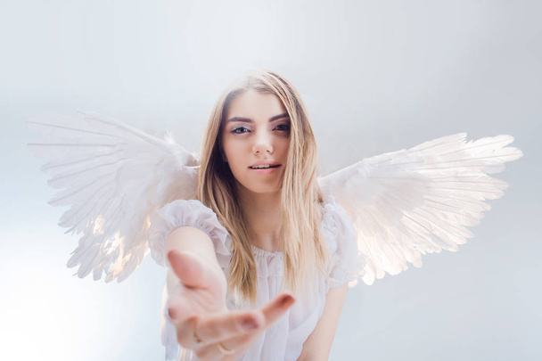 An angel from heaven gives you a hand. Young, wonderful blonde girl in the image of an angel with white wings. - Photo, Image