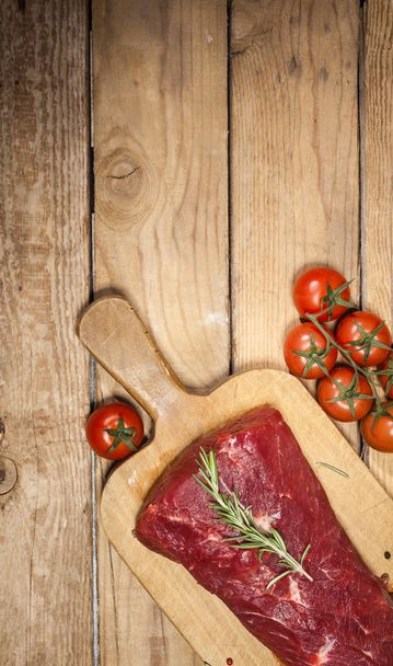 Raw beef steak on a cutting board with rosemary and spices. - Фото, изображение