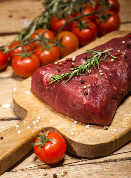 Raw beef steak on a cutting board with rosemary and spices. - Foto, Imagem