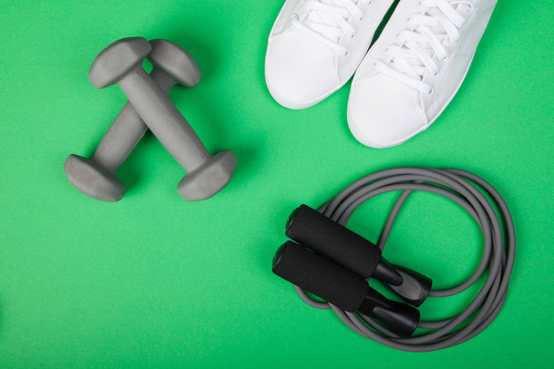 Sport shoes, dumbbells and skipping rope on green background. Top view. Fitness, sport and healthy lifestyle concept. - Valokuva, kuva