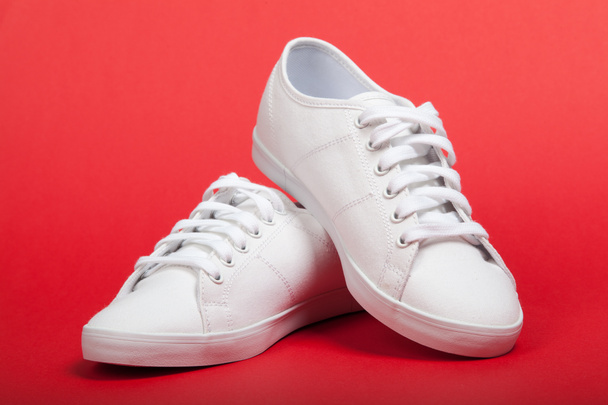 Par de nuevas zapatillas blancas sobre fondo rojo
 - Foto, imagen