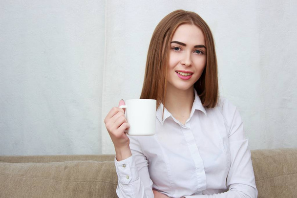 Young beautiful girl with cup of coffee sitting on couch at home. - Foto, Bild