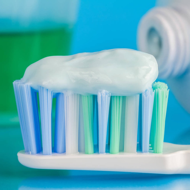Tandpasta op de tandenborstel, groene tandspoeling, tandpasta tube op blauwe achtergrond, focus op voorgrond, macro afbeelding - Foto, afbeelding