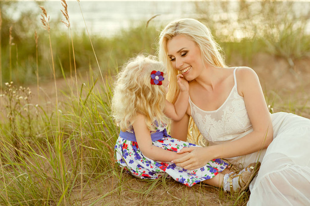 A little blond girl and her mom are smiling on the sand and gras - Fotoğraf, Görsel