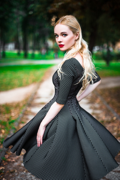 young beautiful blond girl with red lipstick in her big bright eyes and make it in dress posing on the streets , the setting sun trendy clothes - Photo, Image