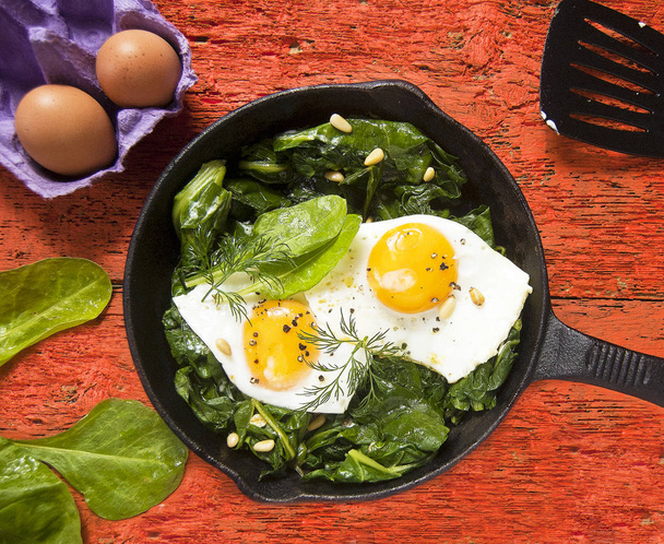 Eggs on spinach on iron skillet  - Photo, Image