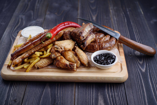 Grilled sausages and chicken with fries on a wooden board - Zdjęcie, obraz