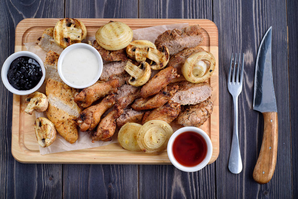 Kızarmış et dilimleri tavuk kanatları, jambon, bir ahşap tahta üzerinde soslu fileto - Fotoğraf, Görsel
