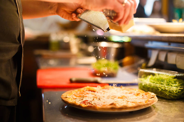 The close-up side photo of the chef grating the cheese on the tasty pizza. - Fotoğraf, Görsel