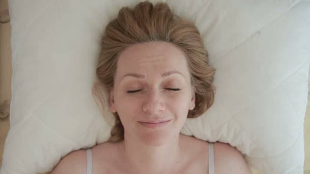 Een vrouw liggend op een bed opent haar ogen en glimlach. Close-up. Van bovenaf bekijken - Video